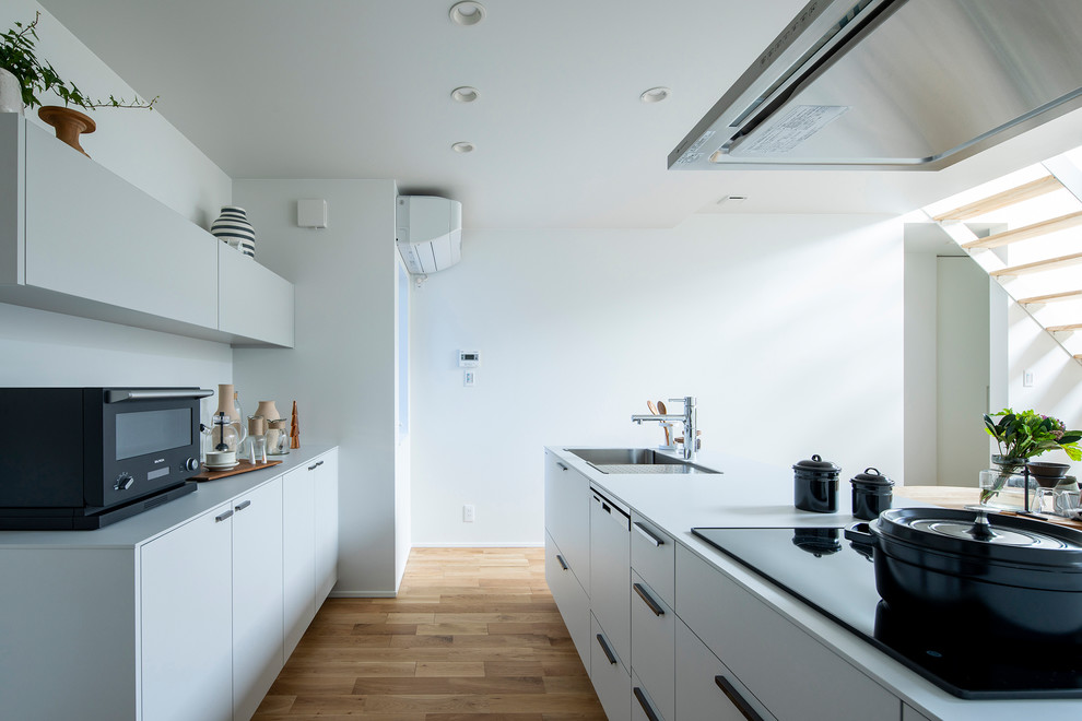 Inredning av ett modernt vit linjärt vitt kök med öppen planlösning, med en undermonterad diskho, luckor med profilerade fronter, vita skåp, vitt stänkskydd, rostfria vitvaror, mellanmörkt trägolv, en halv köksö och beiget golv