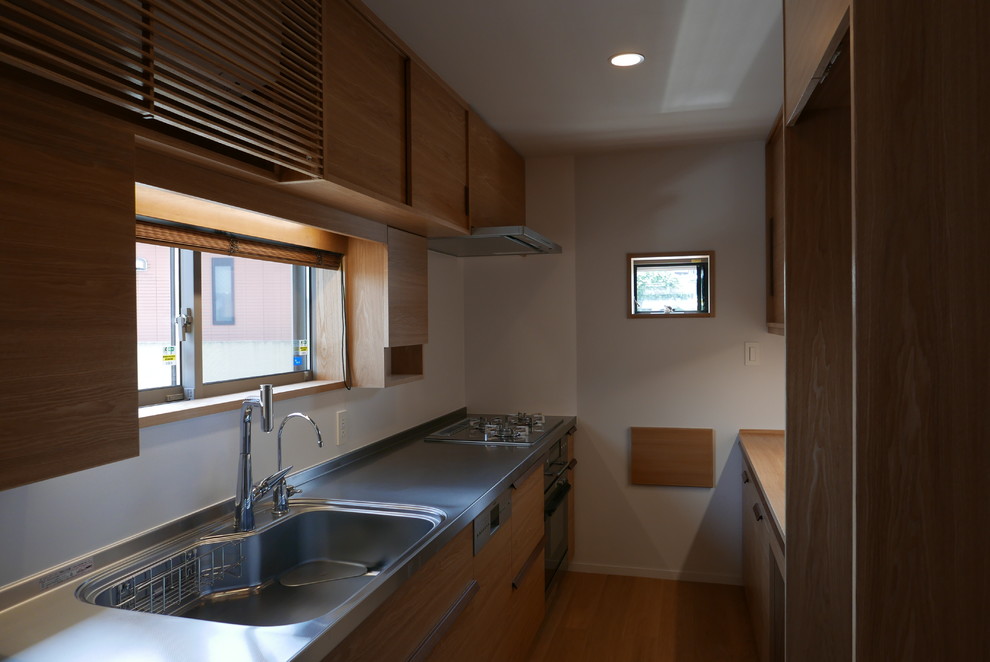 Minimalist galley plywood floor enclosed kitchen photo in Other with an integrated sink, flat-panel cabinets, stainless steel countertops, white backsplash and stainless steel appliances
