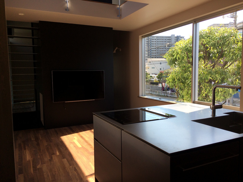 Foto på ett industriellt kök och matrum, med en integrerad diskho, bänkskiva i rostfritt stål, svarta vitvaror, mörkt trägolv, en köksö och brunt golv