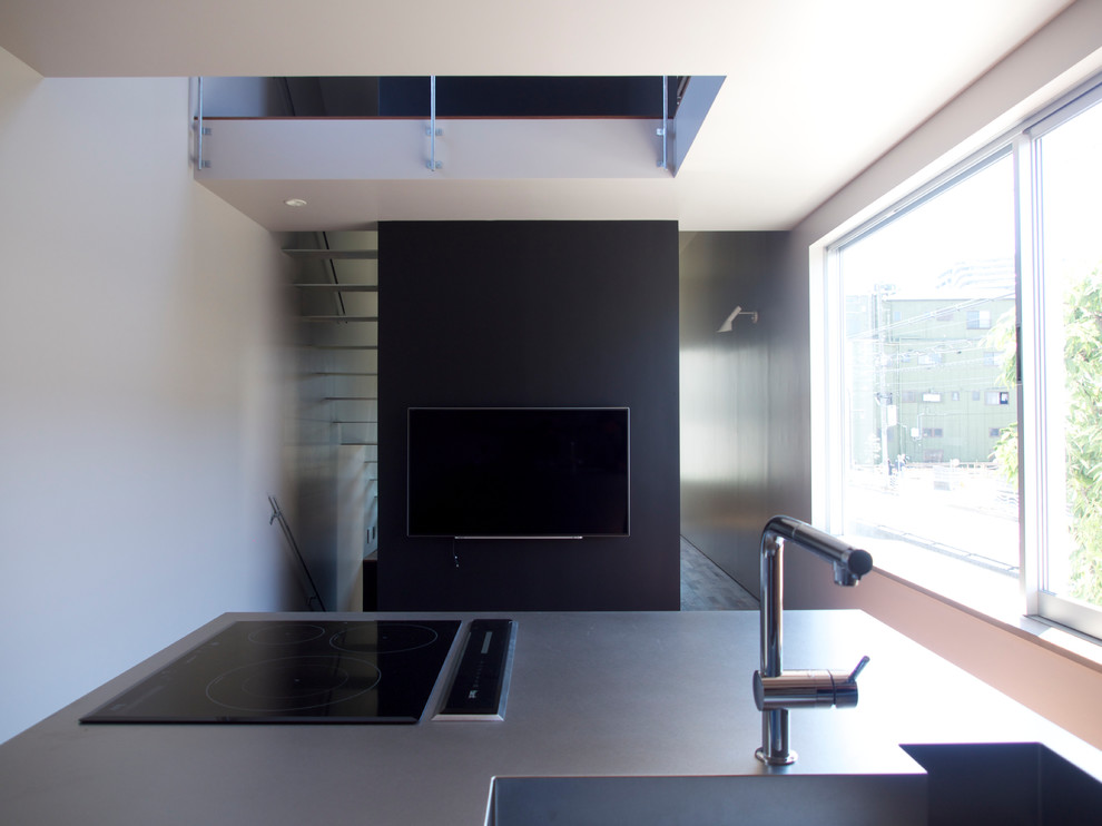 Foto på ett industriellt kök och matrum, med en integrerad diskho, släta luckor, bänkskiva i rostfritt stål, svarta vitvaror, mörkt trägolv, en köksö och brunt golv