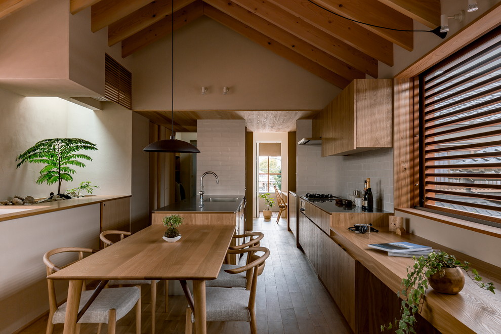 Bild på ett orientaliskt kök med öppen planlösning, med en enkel diskho, släta luckor, skåp i mellenmörkt trä, bänkskiva i rostfritt stål, vitt stänkskydd, mörkt trägolv, en halv köksö och brunt golv