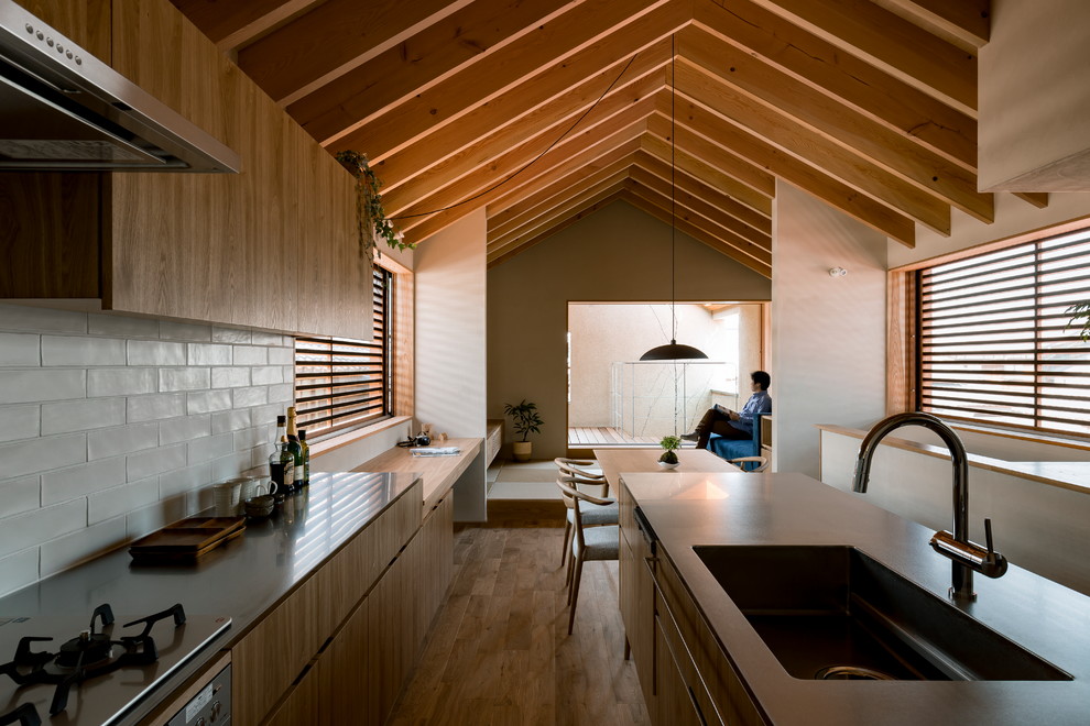Asiatisk inredning av ett kök med öppen planlösning, med en enkel diskho, släta luckor, skåp i mellenmörkt trä, bänkskiva i rostfritt stål, vitt stänkskydd, mörkt trägolv, en halv köksö och brunt golv