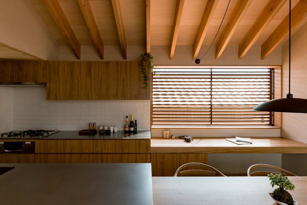 Bild på ett orientaliskt kök med öppen planlösning, med en enkel diskho, släta luckor, skåp i mellenmörkt trä, bänkskiva i rostfritt stål, vitt stänkskydd, mörkt trägolv, en halv köksö och brunt golv