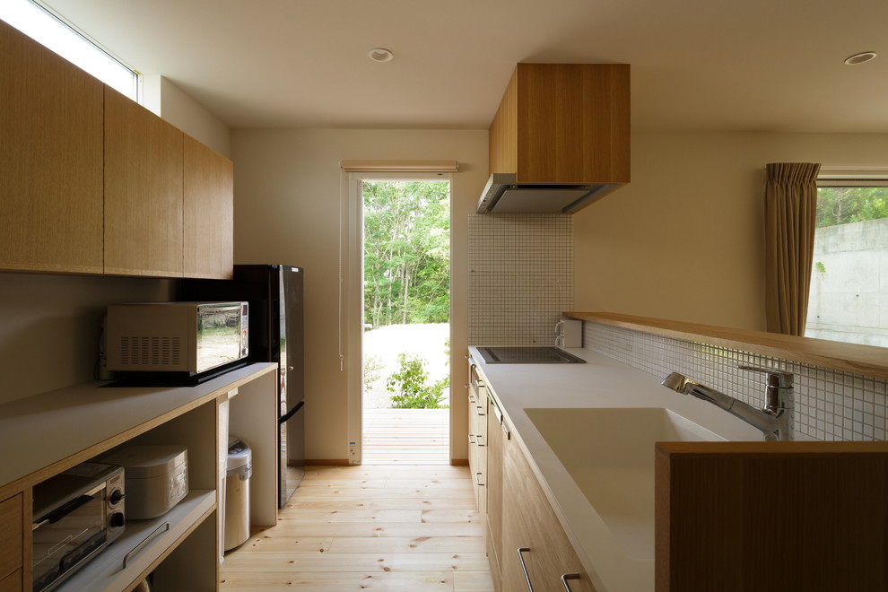 Exempel på ett asiatiskt linjärt kök, med en integrerad diskho, släta luckor, skåp i ljust trä, vitt stänkskydd, stänkskydd i mosaik, rostfria vitvaror, ljust trägolv och en halv köksö