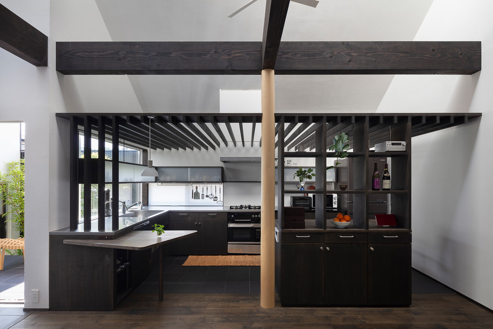 This is an example of a world-inspired u-shaped open plan kitchen in Fukuoka with an integrated sink, flat-panel cabinets, black cabinets, stainless steel worktops, black appliances, a breakfast bar, black floors and grey worktops.