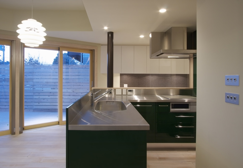 Стильный дизайн: угловая кухня-гостиная в современном стиле с монолитной мойкой, зелеными фасадами, столешницей из нержавеющей стали и светлым паркетным полом - последний тренд