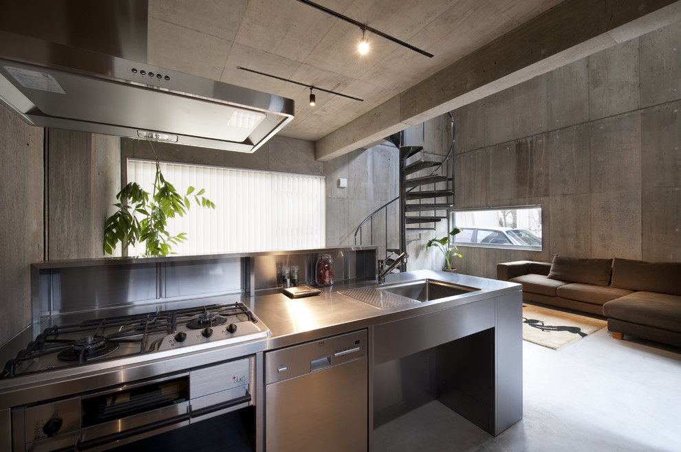 Foto på ett industriellt kök med öppen planlösning, med en enkel diskho, skåp i rostfritt stål, bänkskiva i rostfritt stål, stänkskydd med metallisk yta, en halv köksö och grått golv