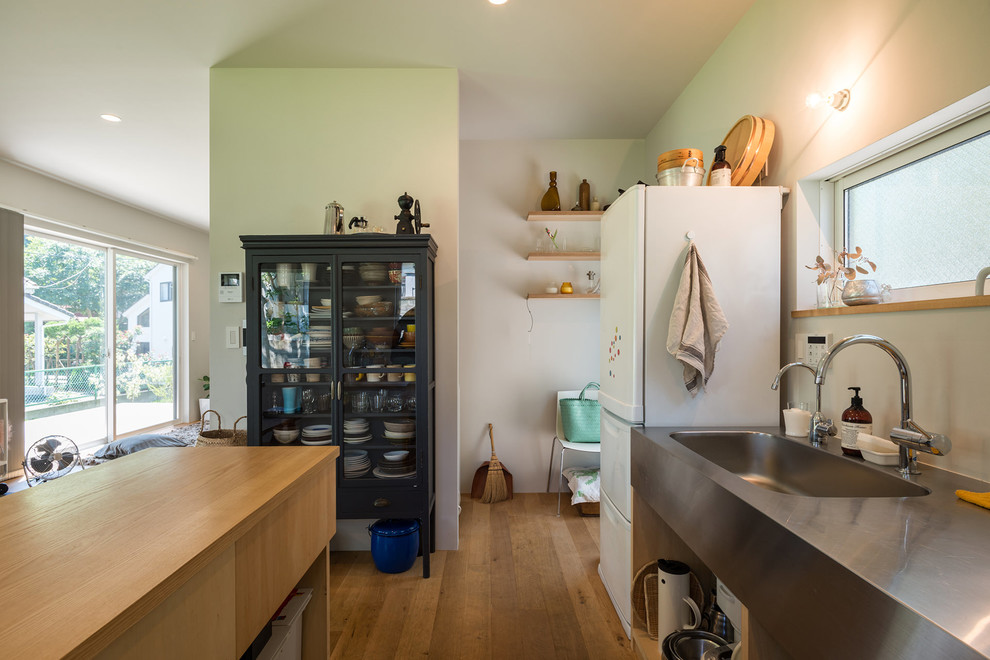 Cette image montre une cuisine parallèle marine avec un évier intégré, un plan de travail en inox, un électroménager en acier inoxydable et un sol en bois brun.