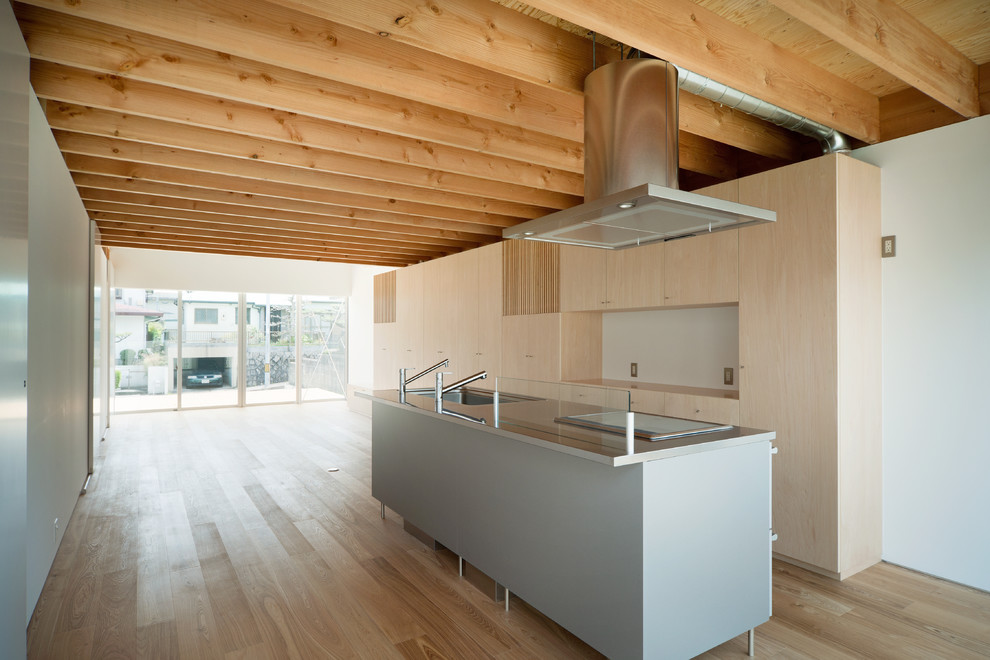 This is an example of a medium sized world-inspired galley open plan kitchen in Nagoya with a submerged sink, flat-panel cabinets, stainless steel cabinets, stainless steel worktops, white splashback, glass sheet splashback, stainless steel appliances, medium hardwood flooring, an island and beige floors.