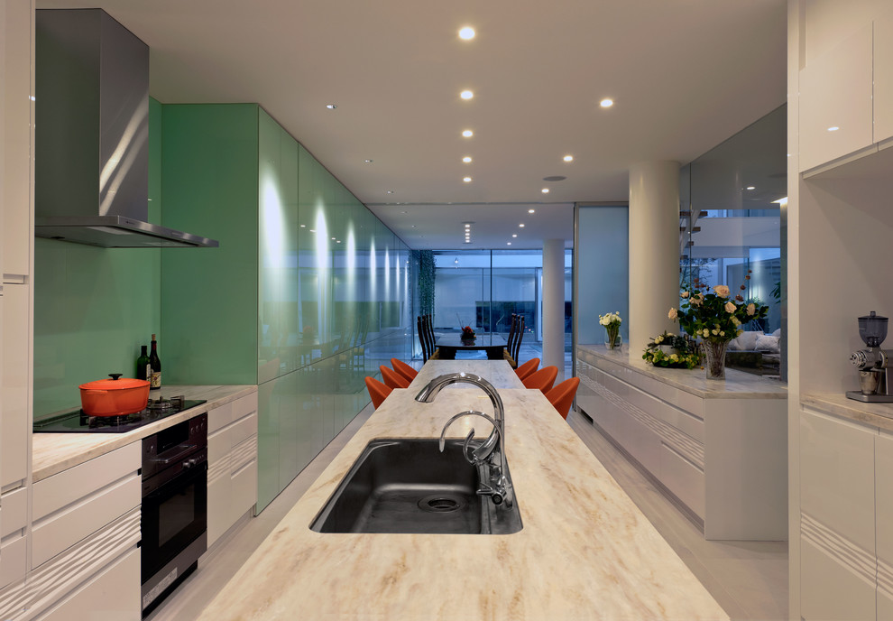 Trendy galley kitchen photo in Tokyo with an undermount sink, flat-panel cabinets, green cabinets, black appliances, an island and green backsplash