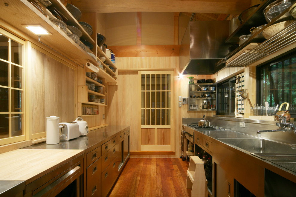 Foto på ett orientaliskt linjärt kök, med en integrerad diskho, släta luckor, skåp i rostfritt stål, bänkskiva i rostfritt stål, mellanmörkt trägolv, en halv köksö och brunt golv