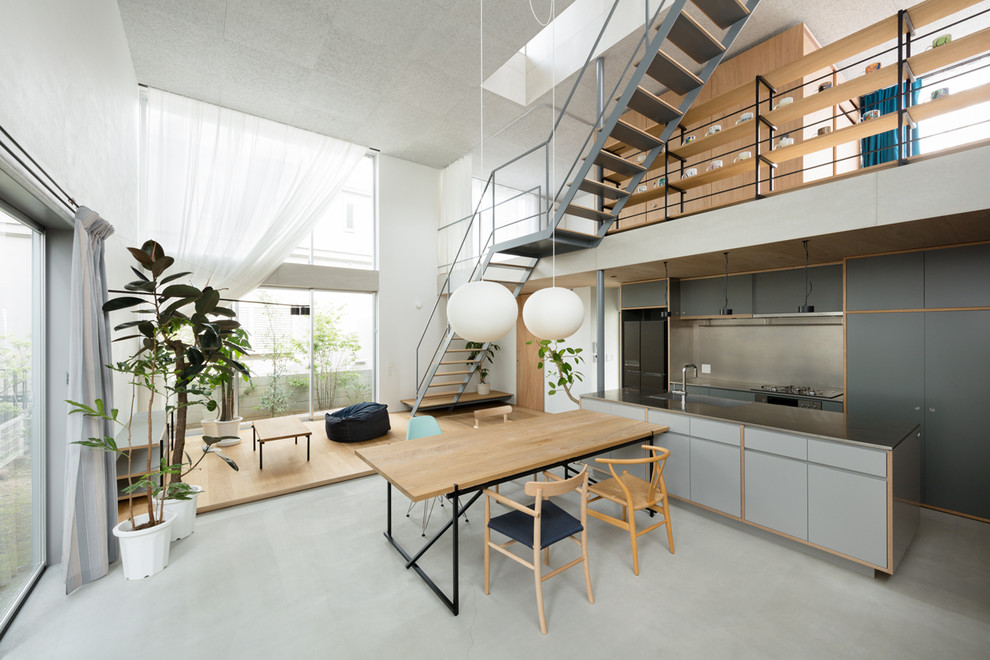 Стильный дизайн: параллельная кухня-гостиная в современном стиле с плоскими фасадами, серыми фасадами, столешницей из нержавеющей стали, серым фартуком, островом, серым полом и бетонным полом - последний тренд