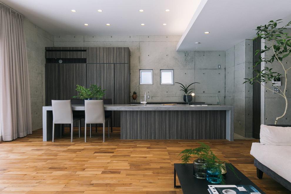 Exemple d'une cuisine parallèle et encastrable asiatique en bois foncé avec un évier encastré, un placard à porte plane, un plan de travail en béton, une crédence grise, un sol en bois brun, îlot, un sol marron et un plan de travail gris.