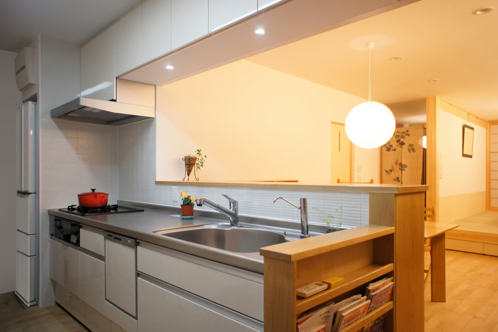 Cette image montre une cuisine ouverte linéaire asiatique de taille moyenne avec un évier intégré, des portes de placard blanches, un plan de travail en inox et parquet clair.
