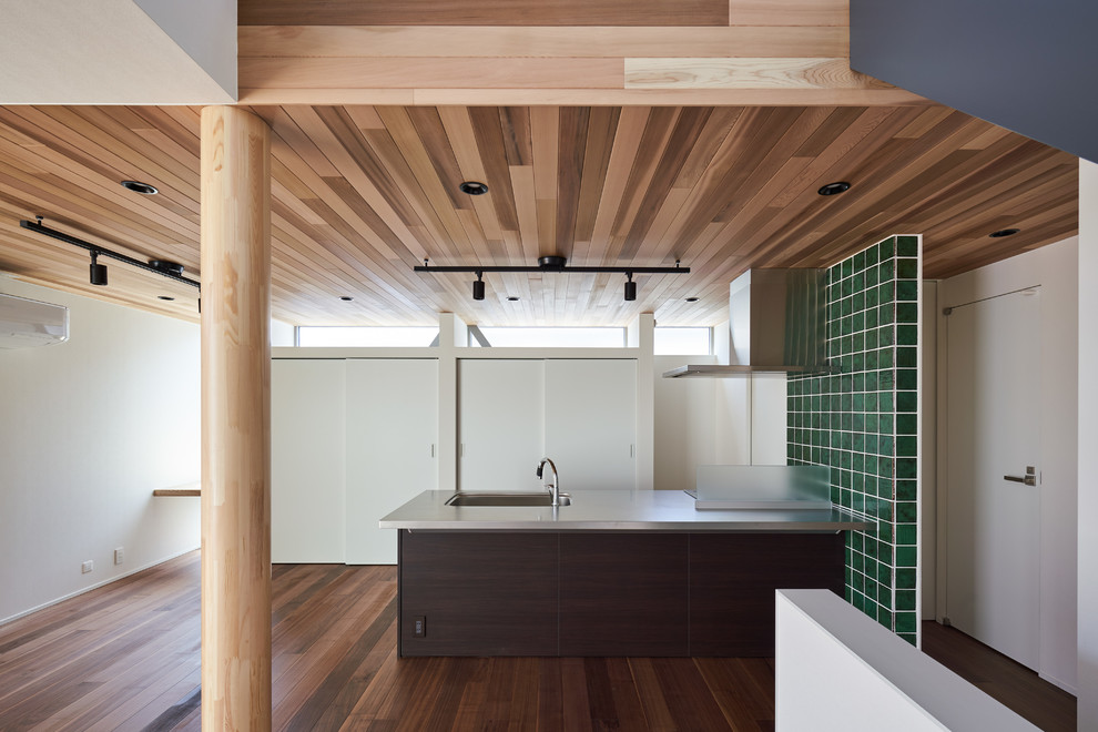 Zweizeilige Moderne Küche mit Unterbauwaschbecken, flächenbündigen Schrankfronten, dunklen Holzschränken, Küchenrückwand in Grün, braunem Holzboden, Kücheninsel, braunem Boden und grauer Arbeitsplatte in Tokio