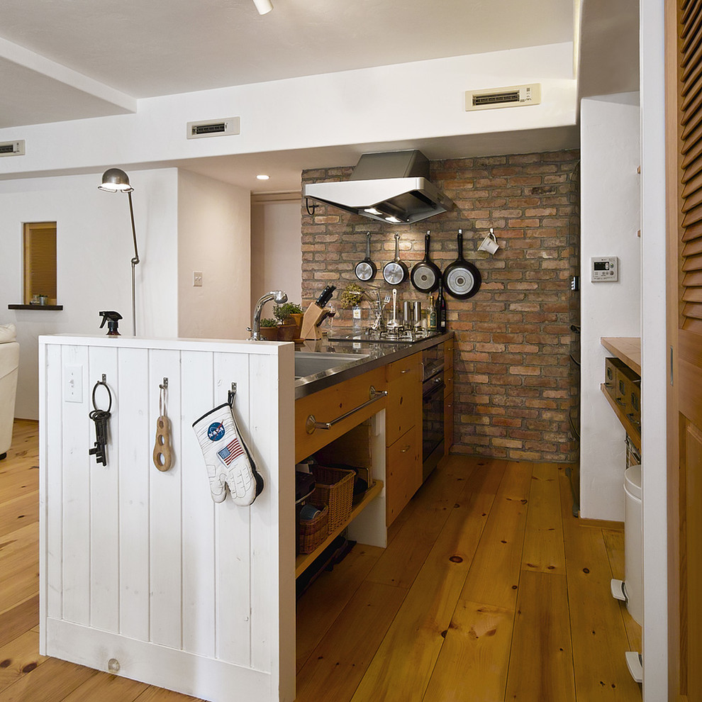 Bild på ett mellanstort funkis linjärt kök med öppen planlösning, med en integrerad diskho, bänkskiva i rostfritt stål, brunt stänkskydd, stänkskydd i tegel, mellanmörkt trägolv och brunt golv