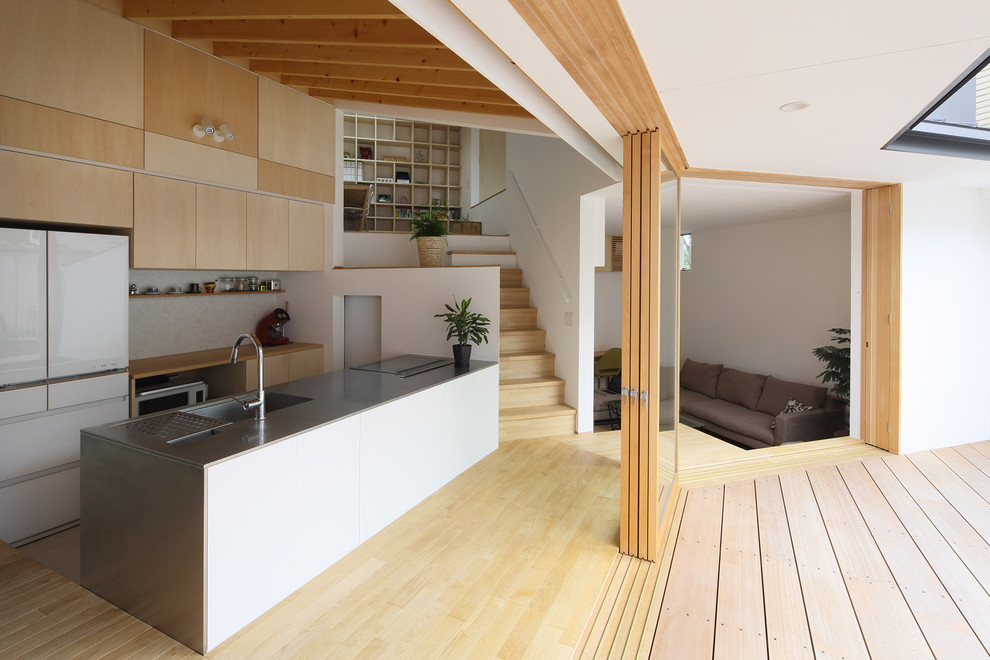Inspiration for a modern single-wall kitchen in Kyoto with a submerged sink, flat-panel cabinets, light wood cabinets, beige splashback, white appliances, light hardwood flooring, a breakfast bar and beige floors.