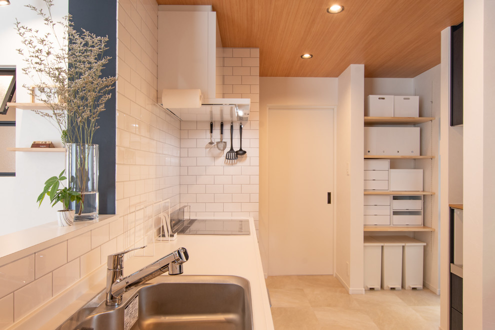 Modern inredning av ett litet vit linjärt vitt kök med öppen planlösning, med en halv köksö, en enkel diskho, släta luckor, skåp i ljust trä, bänkskiva i koppar, vitt stänkskydd, stänkskydd i tunnelbanekakel, vita vitvaror och beiget golv
