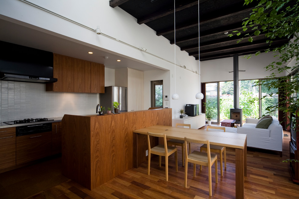 Example of a galley dark wood floor and brown floor open concept kitchen design in Other with an undermount sink, flat-panel cabinets, solid surface countertops, black appliances, an island, medium tone wood cabinets and white backsplash