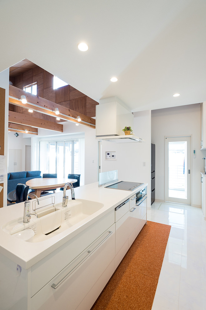 На фото: прямая кухня-гостиная среднего размера в современном стиле с монолитной мойкой, плоскими фасадами, белыми фасадами, фартуком из стекла, черной техникой и полуостровом с