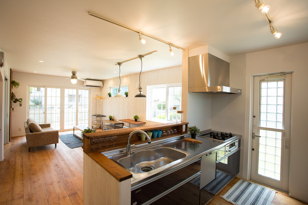Photo of a farmhouse single-wall open plan kitchen in Other with an integrated sink, flat-panel cabinets, brown cabinets, stainless steel worktops, white splashback, medium hardwood flooring, a breakfast bar, brown floors and brown worktops.