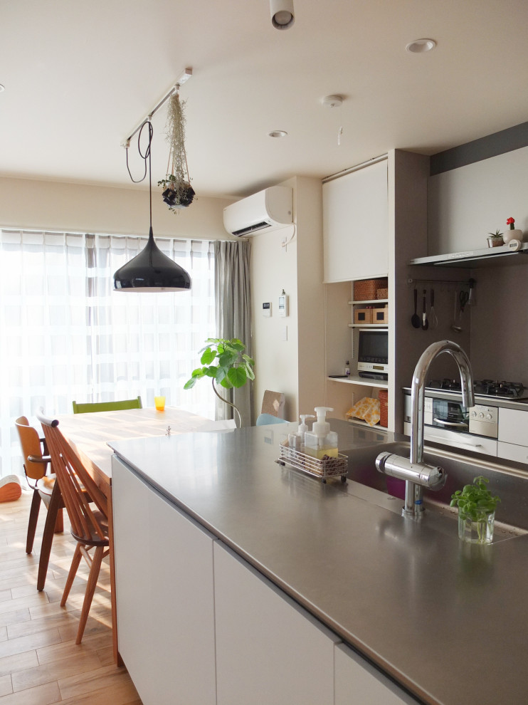 Exempel på ett litet modernt kök, med en integrerad diskho, luckor med profilerade fronter, beige skåp, bänkskiva i rostfritt stål, mellanmörkt trägolv, en köksö och brunt golv