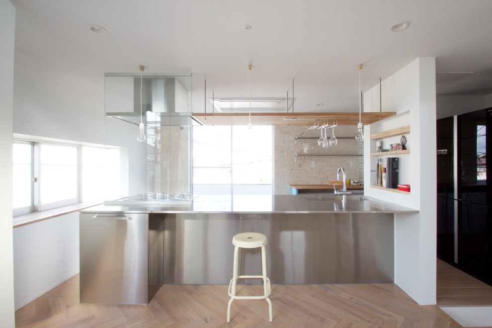 Cette image montre une cuisine linéaire design en inox avec un évier intégré, un plan de travail en inox, parquet peint, îlot et un sol marron.