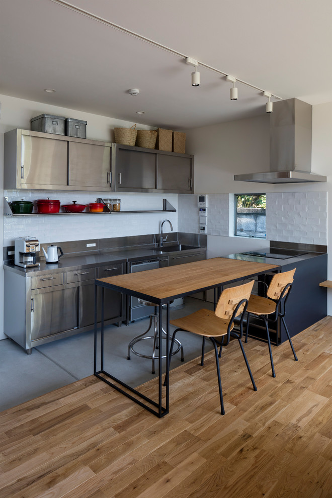 Design ideas for an urban galley kitchen/diner in Other with an integrated sink, flat-panel cabinets, stainless steel cabinets, white splashback, metro tiled splashback, no island, stainless steel worktops and medium hardwood flooring.