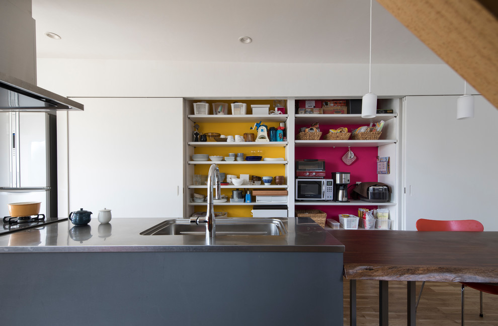Exempel på ett modernt grå grått kök, med en integrerad diskho, släta luckor, vita skåp, bänkskiva i rostfritt stål, gult stänkskydd, mellanmörkt trägolv, en köksö och brunt golv