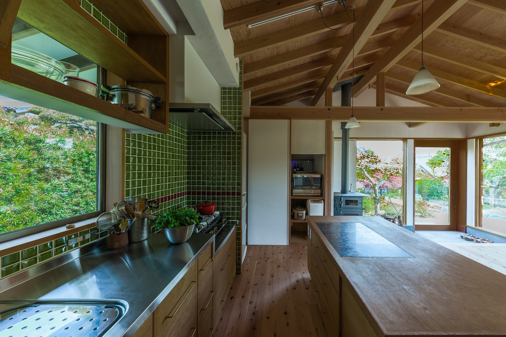 Cette image montre une cuisine linéaire asiatique en bois vieilli avec un évier intégré, un plan de travail en inox, une crédence verte, une crédence en carreau de porcelaine, un sol en bois brun, un sol marron, un placard à porte plane et îlot.