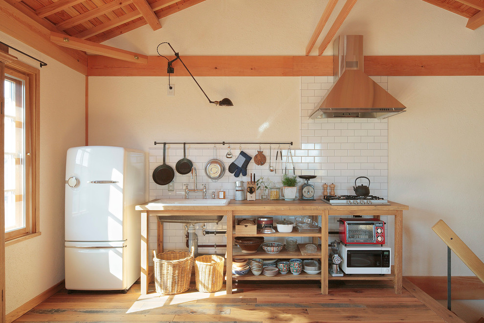 Foto de cocina campestre con fregadero bajoencimera, armarios abiertos, encimera de madera, salpicadero blanco, suelo de madera en tonos medios, una isla, puertas de armario de madera clara y electrodomésticos de acero inoxidable