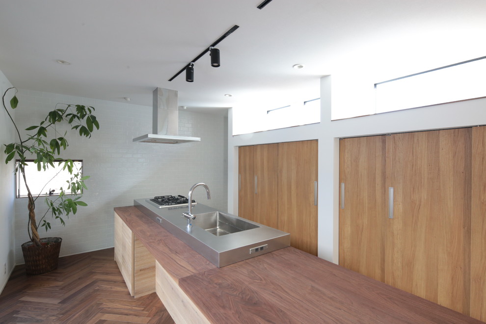 Foto de cocina minimalista con armarios con paneles lisos, puertas de armario de madera en tonos medios, encimera de acero inoxidable, una isla, encimeras grises y fregadero integrado