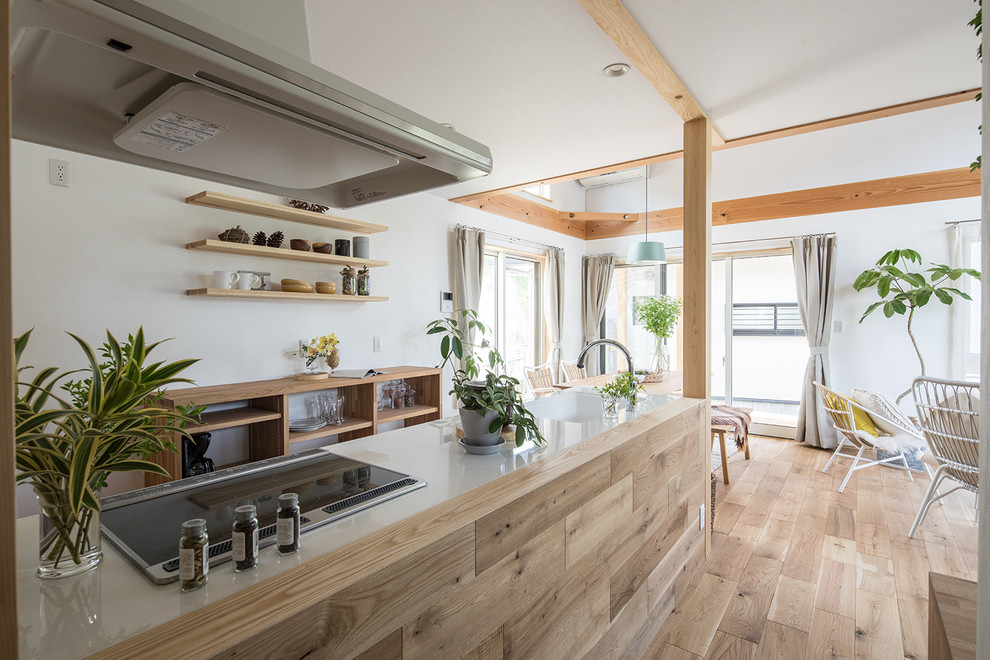 Réalisation d'une cuisine ouverte parallèle nordique en bois clair avec un sol en bois brun, îlot, un plan de travail blanc, un évier intégré, un placard sans porte, une crédence blanche et un sol beige.