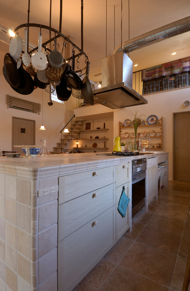 他の地域にあるカントリー風のおしゃれなキッチン (インセット扉のキャビネット、淡色木目調キャビネット、タイルカウンター、シルバーの調理設備) の写真