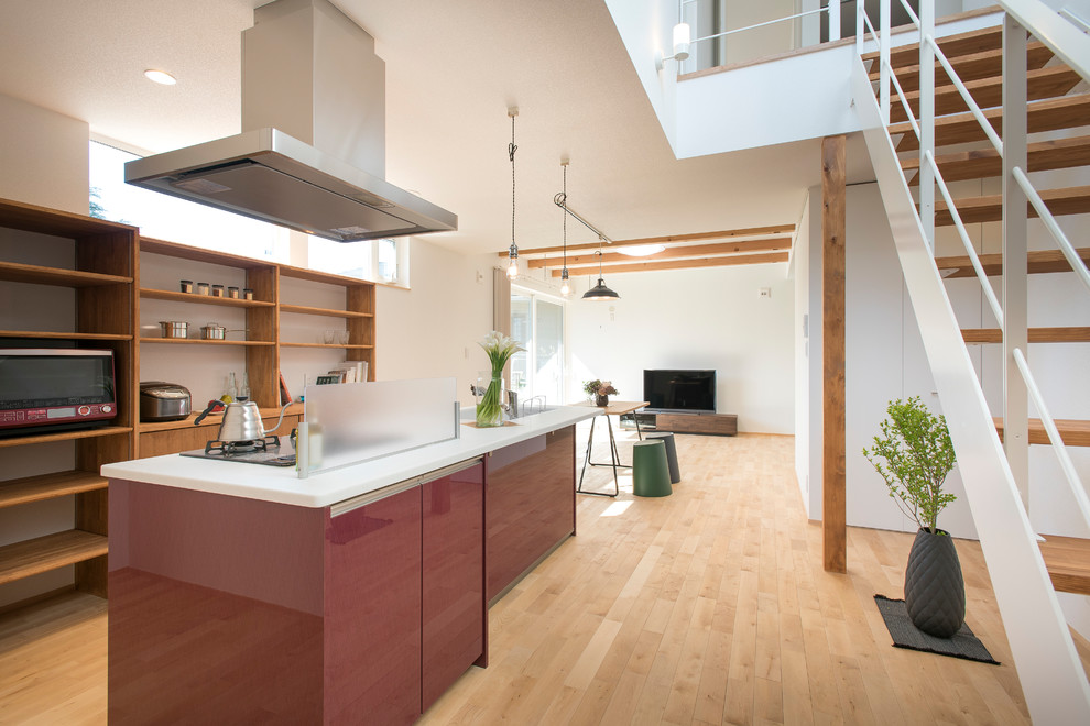 На фото: параллельная кухня-гостиная в восточном стиле с монолитной мойкой, открытыми фасадами, светлым паркетным полом, островом и коричневым полом с