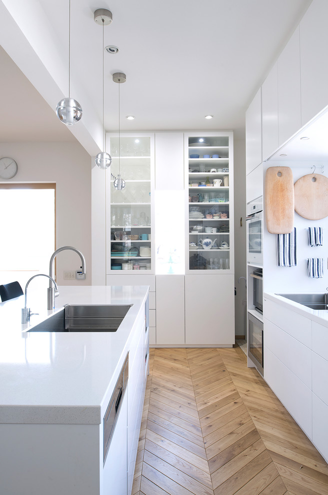 北欧スタイルのおしゃれなキッチン (アンダーカウンターシンク、白いキャビネット、白いキッチンパネル、白い調理設備、淡色無垢フローリング、茶色い床、フラットパネル扉のキャビネット、白いキッチンカウンター) の写真