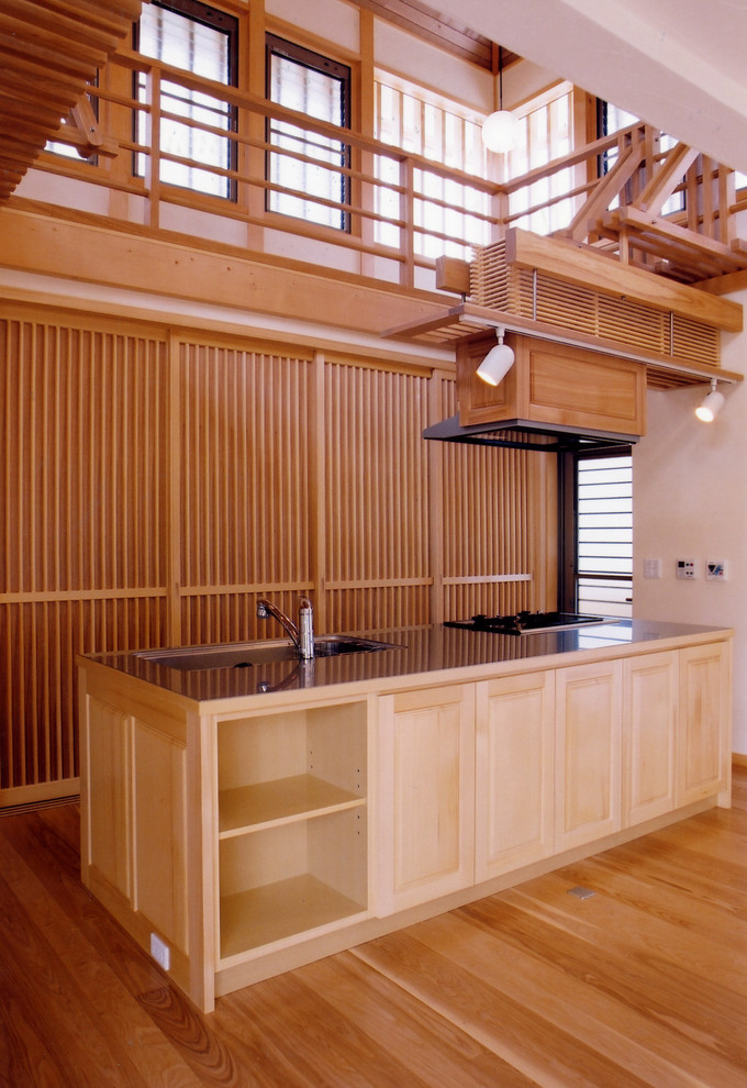 Diseño de cocina lineal asiática con armarios con paneles con relieve, puertas de armario de madera clara, suelo de madera en tonos medios, una isla, salpicadero beige y electrodomésticos de colores
