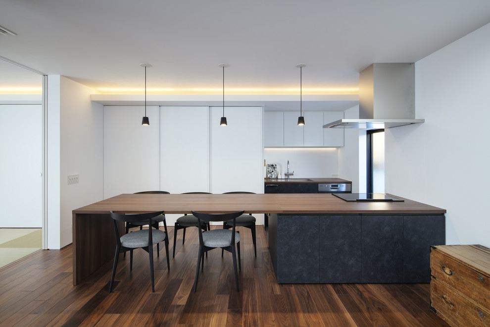 Contemporary galley kitchen in Other with flat-panel cabinets, black cabinets, wood worktops, white splashback, dark hardwood flooring, a breakfast bar, brown floors and brown worktops.