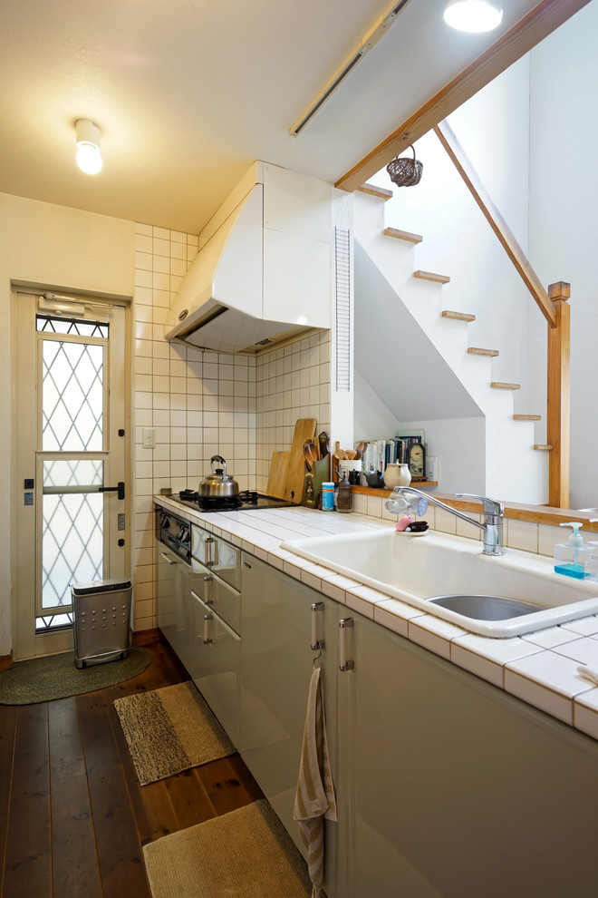 他の地域にある北欧スタイルのおしゃれなキッチン (ドロップインシンク、フラットパネル扉のキャビネット、緑のキャビネット、タイルカウンター、白いキッチンパネル、セラミックタイルのキッチンパネル、濃色無垢フローリング、茶色い床) の写真