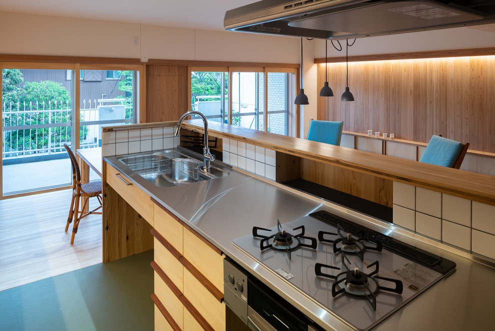 Foto på ett amerikanskt kök, med en enkel diskho, luckor med profilerade fronter, skåp i mellenmörkt trä, bänkskiva i rostfritt stål, stänkskydd i trä, linoleumgolv, en köksö och grönt golv