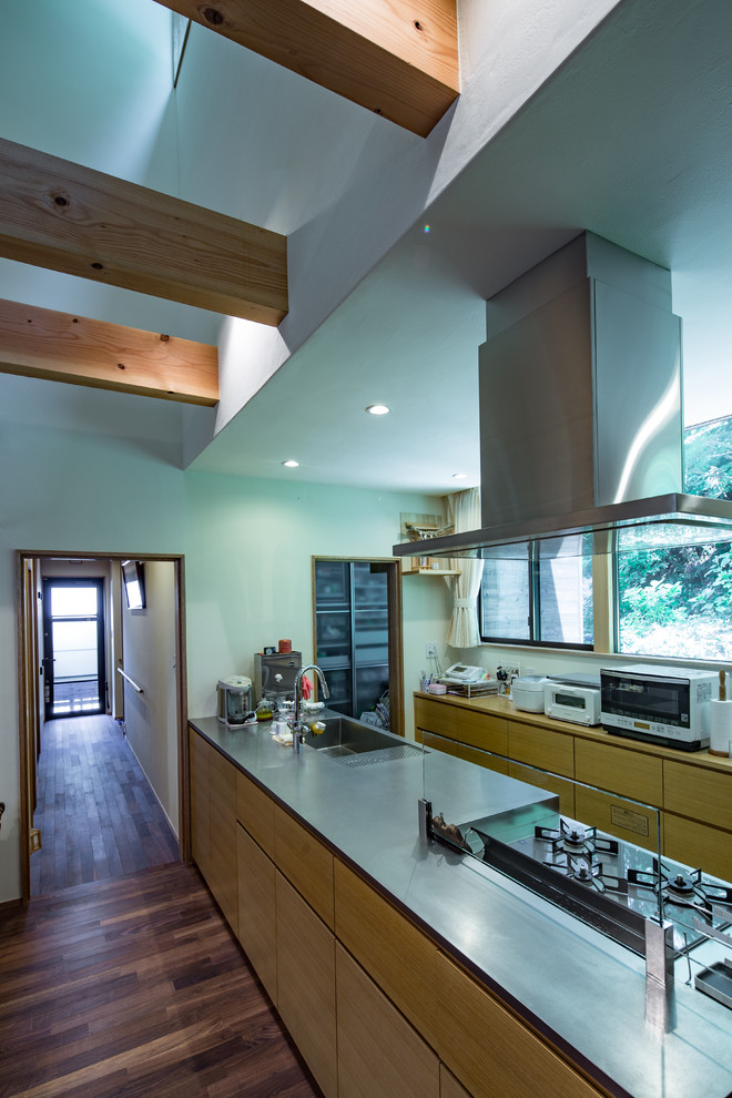 Modelo de cocina de estilo zen abierta con encimera de acero inoxidable, salpicadero de madera, suelo de madera oscura y una isla