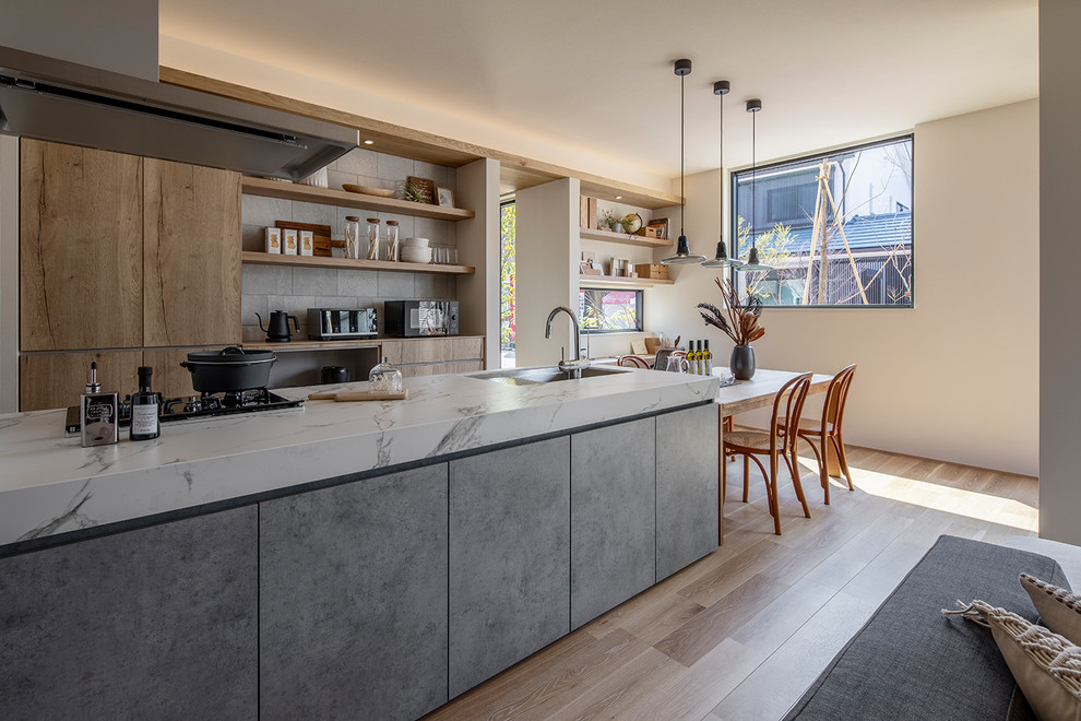 Photo of a contemporary single-wall open plan kitchen in Tokyo with a submerged sink, beaded cabinets, grey cabinets, engineered stone countertops, stainless steel appliances, light hardwood flooring, a breakfast bar, beige floors and white worktops.