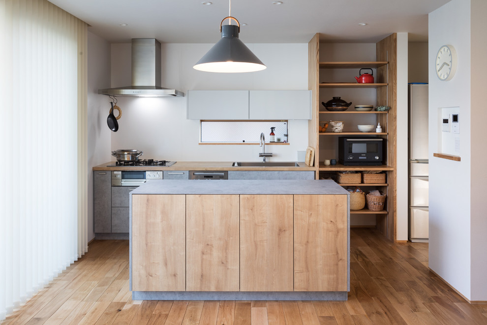 Bild på ett nordiskt kök, med rostfria vitvaror, en köksö, en enkel diskho, släta luckor, grå skåp, träbänkskiva och ljust trägolv