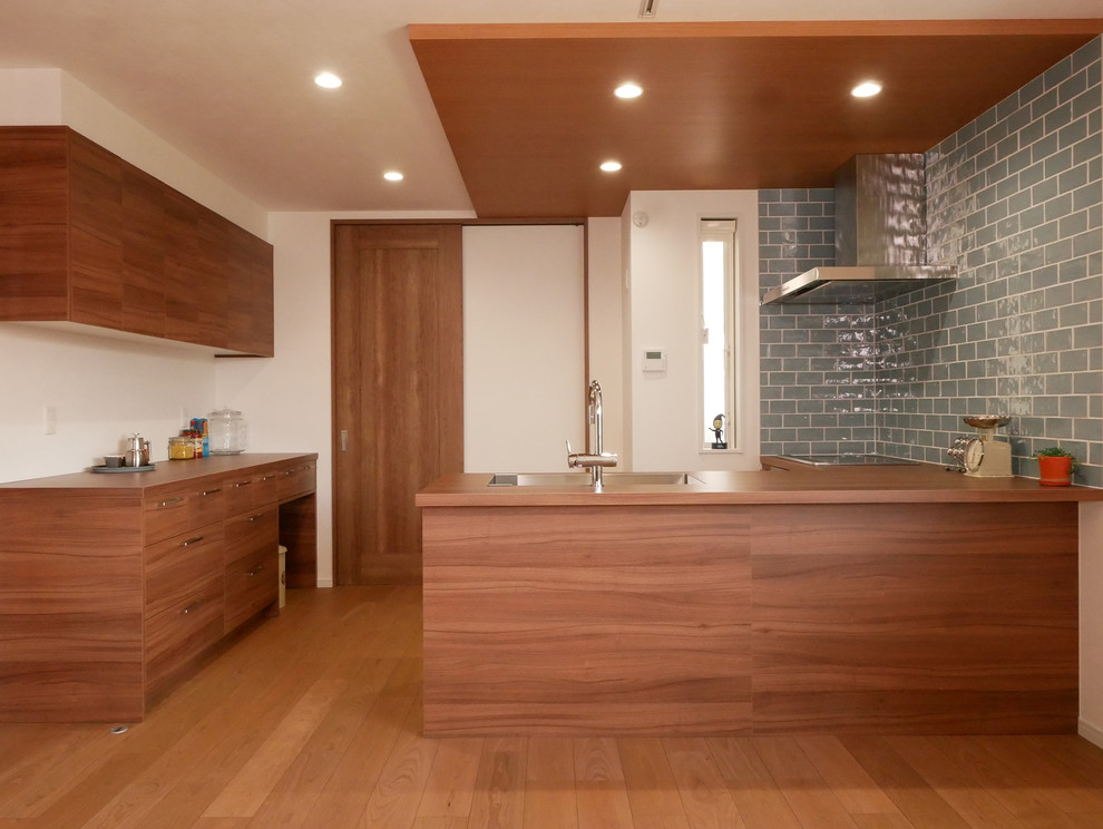 Example of a trendy l-shaped brown floor open concept kitchen design in Tokyo with an undermount sink, beaded inset cabinets, medium tone wood cabinets, blue backsplash, subway tile backsplash, stainless steel appliances, a peninsula and brown countertops