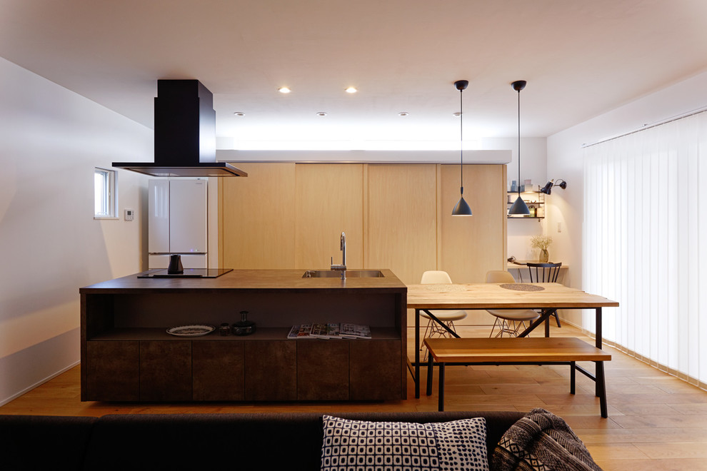Example of a zen single-wall brown floor and medium tone wood floor open concept kitchen design in Tokyo with an undermount sink, flat-panel cabinets, distressed cabinets, gray backsplash, black appliances and an island