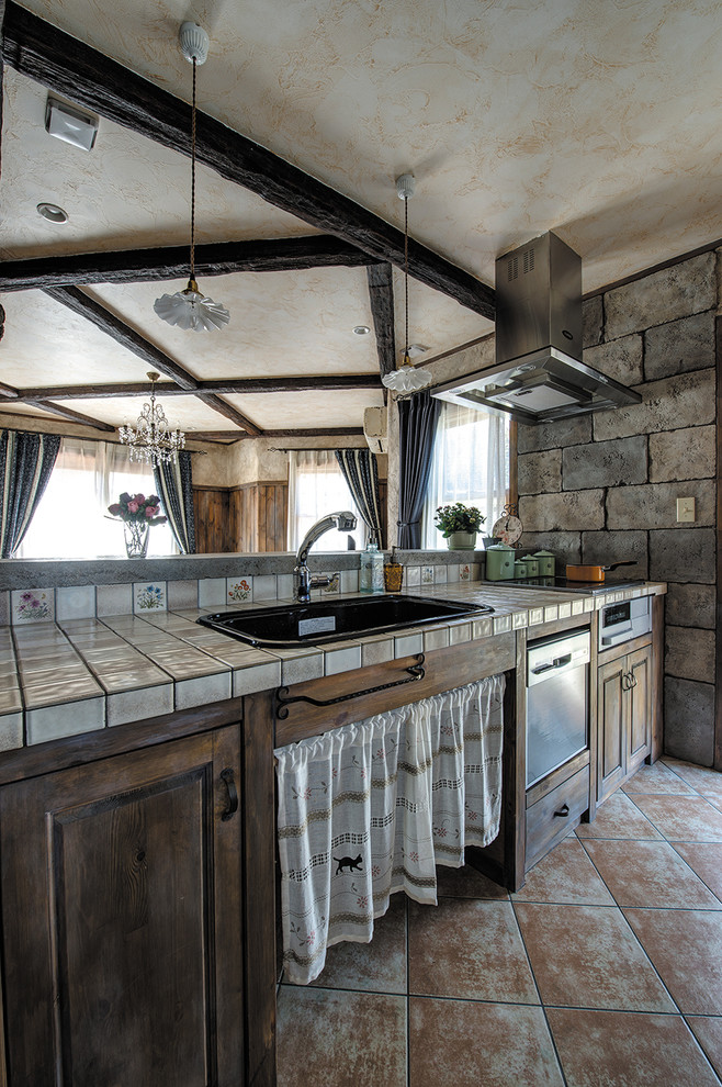 Foto på ett vintage linjärt kök med öppen planlösning, med en nedsänkt diskho, luckor med infälld panel, skåp i slitet trä, kaklad bänkskiva, klinkergolv i terrakotta, en halv köksö och brunt golv
