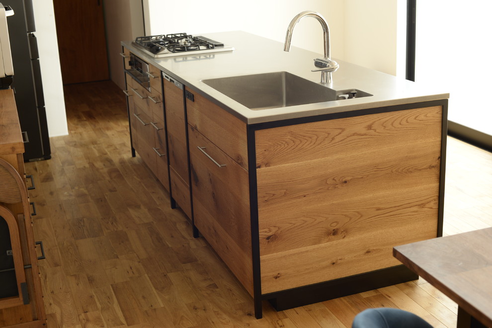 Exempel på ett industriellt grå linjärt grått kök med öppen planlösning, med en integrerad diskho, släta luckor, bruna skåp, bänkskiva i rostfritt stål, rostfria vitvaror, mellanmörkt trägolv, en köksö och brunt golv