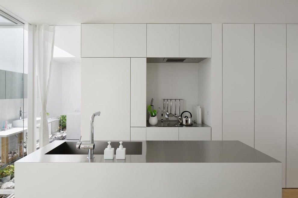 Zweizeilige Moderne Küche mit integriertem Waschbecken, flächenbündigen Schrankfronten, weißen Schränken, Edelstahl-Arbeitsplatte, Kücheninsel, Küchengeräten aus Edelstahl und hellem Holzboden in Tokio