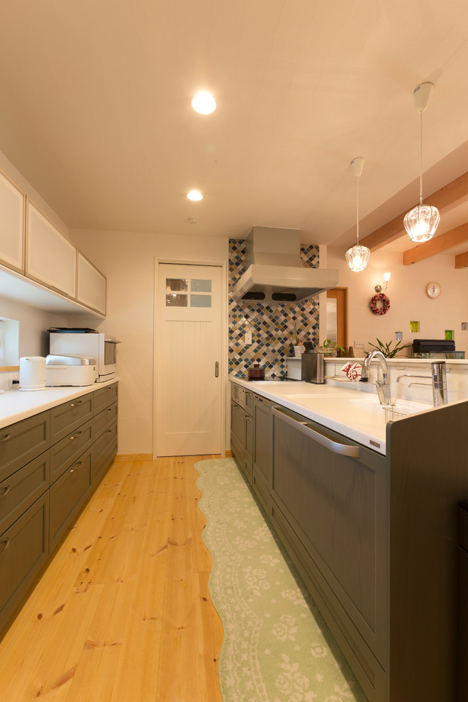 Foto på ett orientaliskt linjärt kök med öppen planlösning, med en integrerad diskho, luckor med infälld panel, gröna skåp, vitt stänkskydd, mellanmörkt trägolv, brunt golv och en halv köksö