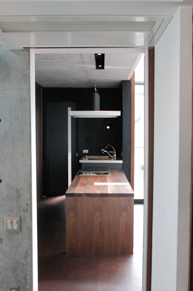 Modern inredning av ett mellanstort kök, med en integrerad diskho, släta luckor, bruna skåp, träbänkskiva, svart stänkskydd, svarta vitvaror, korkgolv, en halv köksö och brunt golv